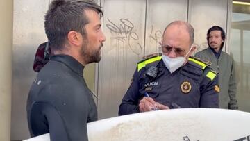 Un agente de policía de la Guàrdia Urbana de Barcelona identifica a un surfista en la ciudad de Barcelona (con tabla de surf y neopreno) por estar surfeando durante las olas de un temporal en la Barceloneta el 10 de noviembre del 2021.