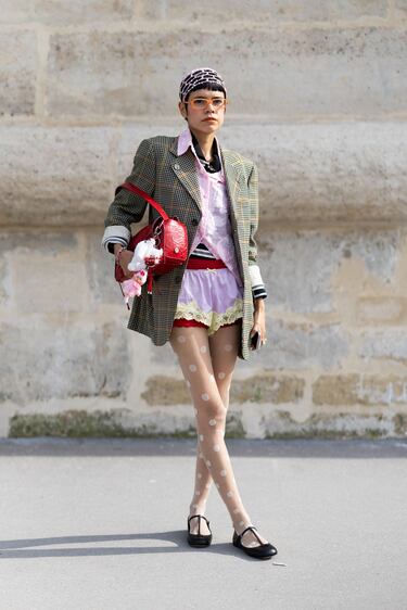 Lorena Chavez Delion luce un sombrero rosa de cuentas, gafas naranjas, un polo de rayas blancas y negras, una camisa rosa de encaje, shorts rojos, shorts rosas y amarillos, medias beige con lunares, bailarinas negras de cuero, un bolso rojo de cuero y un blazer de cuadros beige y grises en el desfile de Dior durante la Semana de la Moda de París Primavera/Verano 2026, el 1 de octubre de 2025.