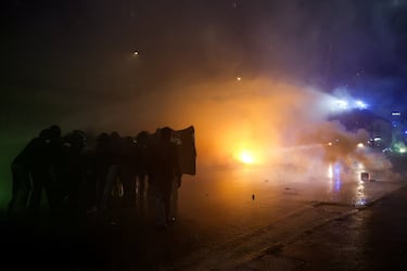 Los manifestantes se ponen a cubierto mientras la policía usa un cañón de agua contra ellos, mientras intentaban bloquear una carretera que conduce a la Arena Santa Giulia, el día de una protesta contra el impacto ambiental, económico y social de los Juegos Olímpicos de Invierno Milano-Cortina 2026.