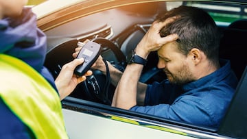 drink and drive concept - sad drunk man sitting in the car after police alcohol test with alcometer