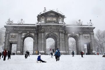 Varias personas caminan junto a la Puerta de Alcalá de Madrid.