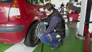 Un trabajador de un taller protegido con una mascarilla arregla la rueda de un coche.