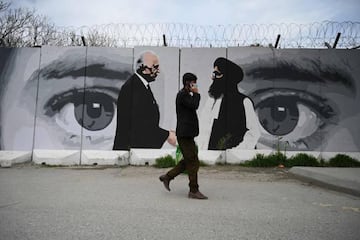 A man wearing a facemask as a precautionary measure against the COVID-19 novel coronavirus walk past a wall painted with images of US Special Representative for Afghanistan Reconciliation Zalmay Khalilzad (L) and Taliban co-founder Mullah Abdul Ghani Bara
