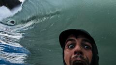 El fot&oacute;grafo de surf Jose Dopico haciendo una mueca de sorpresa con la c&aacute;mara, en modo selfie, ante una ola que le rompe justo encima. 