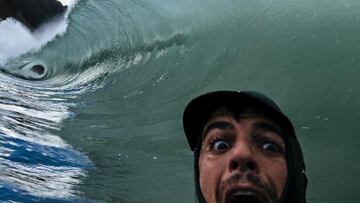 El fotógrafo de surf Jose Dopico haciendo una mueca de sorpresa con la cámara, en modo selfie, ante una ola que le rompe justo encima.