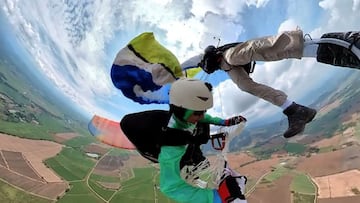 Dos paracaidistas enganchados en el aire con campos de Colombia debajo y el cielo nublado.