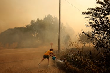 Un residente local vierte agua de un cubo durante un incendio forestal en Congosta, España.