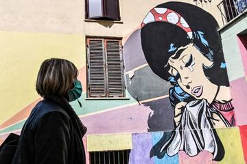 A resident wearing a protective mask and gloves, walks past a mural in the Trullo district of Rome, on April 16, 2020, as some shops reopen following a government decision, during the country's lockdown aimed at curbing the spread of the COVID-19 outbreak