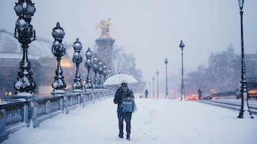 Una persona se protege de la nieve que cae bajo una sombrilla en el Puente Alexandre III cubierto de nieve en París.