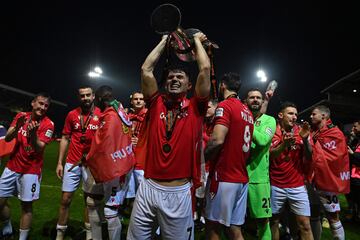 Wrexham's Welsh defender Jordan Davies (C) holds the trophy as players celebrate on the pitch after the English National League