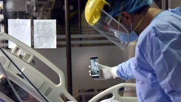 BOGOTA, COLOMBIA - AUGUST 28: A health worker wearing personal protective equipment (PPE) makes a video conference with his cell phone between a patient with Covid-19 and his wife in the Intensive Care Unit at de La Samaritana University Hospital on August 28, 2020 in Bogota, Colombia. According to WHO reports, Colombia counts over 582,000 positive coronavirus cases and more than 18,400 deaths. (Photo by Guillermo Legaria/Getty Images)