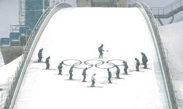 Vista general de los trabajadores acondicionando la pista en medio de la nevada antes de la prueba.