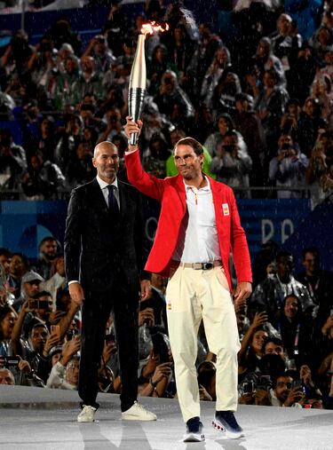 El tenista espa?ol, Rafa Nadal, con la antorcha olmpica ante la atenta mirada del exfutbolista del Real Madrid y seleccin francesa, Zinedine Zidane.