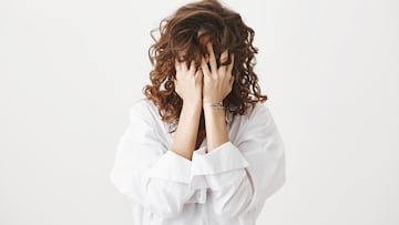 Studio portrait of tired or bothered woman hiding face in her curly hair and holding hands on it, expressing exhaustion or just being childish, standing over gray background. I am not seeing you.