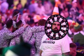 Este aficionado o es un insconciente o la novia de cuyo amor alardea en la camiseta tiene superpoderes para protegerle de cualquier peligro. Si no, no se entiende que acudiera de semejante guisa al Mundial de dardos que se disputa en Londres (Inglaterra), donde la puntería de los participantes para acertar en el centro de la diana se da por hecho.