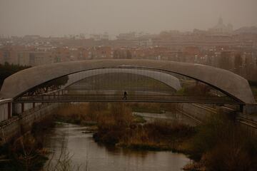 Un hombre cruza un puente sobre el río Manzanares rodeado del polvo sahariano traído por la tormenta Celia.