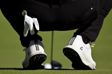 Vista detallada de los zapatos del español Jon Rahm mientras alinea un putt en el cuarto green.