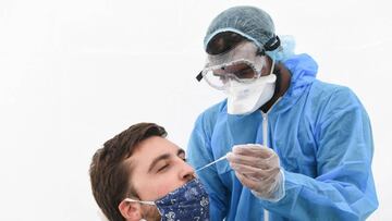 A medical worker wearing protective equipment uses a swab to do a PCR test for Covid-19 on a man wearing a face mask on August 31, 2020, at a testing booth in Montreuil, near Paris. (Photo by ALAIN JOCARD / AFP)