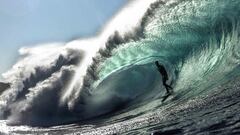 Un surfista surfea una gran ola en forma de tubo, con el labio de la misma haci&eacute;ndole sombra y visto desde el agua. 