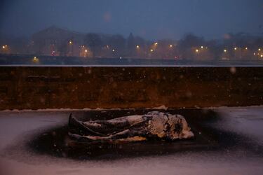 Una persona sin hogar yace en un respiradero en el Puente Alexandre III cubierto de nieve en París mientras el clima invernal con nieve y temperaturas frías golpea una parte del país.