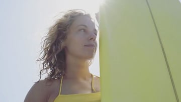 Una surfista con su tabla de surf y el sol detr&aacute;s de la tabla en un plano de la pel&iacute;cual Femme Ocean. 