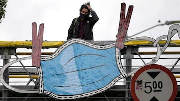 A man stands next to a giant image of a facemask hanging from a pedestrian bridge as part of an awareness campaign called "The mask, like the clothes: tight!" of the mayoralty against the spread of COVID-19 in Bogota, on April 14, 2021. (Photo by Raul ARBOLEDA / AFP)