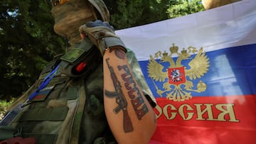 A participant stands next to a Russian state flag at an exhibition showcasing volunteers' product range, manufactured to supply the needs of service members involved in Russia's military campaign in Ukraine, in Yevpatoriya, Crimea, July 29, 2023. A tattoo reads: "Russia". REUTERS/Alexey Pavlishak