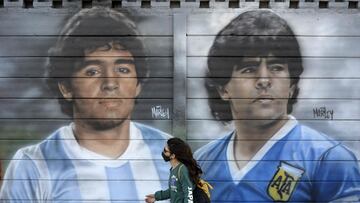 A person passes by murals painted by artist Marley outside the Diego Armando Maradona stadium as people are gathering to commemorate the Argentine legend&#039;s second goal against England during the FIFA World Cup Mexico 1986 on its 35th anniversary, in Buenos Aires on June 22, 2021. (Photo by Juan MABROMATA / AFP) / RESTRICTED TO EDITORIAL USE - MANDATORY MENTION OF THE ARTIST UPON PUBLICATION - TO ILLUSTRATE THE EVENT AS SPECIFIED IN THE CAPTION