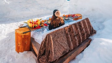 Una mujer desayuna en la cama sobre la nieve en Italia. 