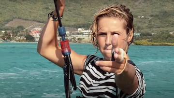 Pippa van Iersel haciendo el gesto con los dedos de disparar mientras agarra su cometa, con el mar y las montañas de fondo.