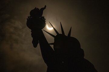 La luna cubre parcialmente el sol detrás de la Estatua de la Libertad durante un eclipse solar en la Isla de la Libertad.