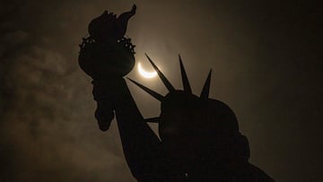 La luna cubre parcialmente el sol detrás de la Estatua de la Libertad durante un eclipse solar en la Isla de la Libertad.