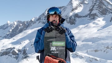 El snowboarder Fidel Alonso posando con su tabla de snowboard, con pegatinas de Europcar, Aramón y Salomon, frente a las montañas nevadas de Cerler (Pirineo Aragonés), en 2023.