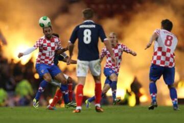 Darijo Srna (L) de Croacia cabecea la pelota, mientras unas bengalas arden en el fondo durante el partido de Escocia y Croacia durante la clasificación para el Mundial 2014.