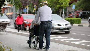 Un hombre pasea a una persona de edad avanzada en silla de ruedas durante su franja horaria permitida en la desescalada por la crisis del Covid-19 donde aquellos mayores de 70 años pueden salir a la vía pública de 10.00 a 12.00 horas y de 19.00 a 20.00 ho