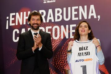 La presidenta de la Comunidad de Madrid, Isabel Díaz Ayuso, recibe una camiseta conmemorativa de manos del capitán del Real Madrid de baloncesto Sergio Llull.
