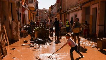 Un niño ayuda a retirar fango de las calles de uno de los municipios valencianos devastados por la DANA.