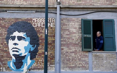 A mural in tribute to Diego Maradona is seen on a wall as a man looks out of a window in Naples REUTERS/Yara Nardi