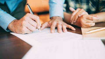Hand of senior male candidate holding pen and filling in application form together with woman at table. Senior partner signing contract