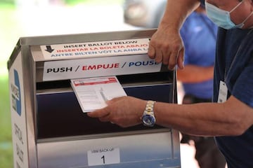 DORAL, FLORIDA - OCTOBER 14: A poll workers places Vote-by Mail ballots into a ballot box set up at the Miami-Dade Election Department headquarters on October 14, 2020 in Doral, Florida.