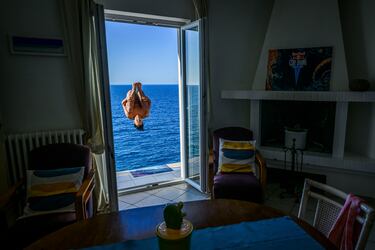 En esta original fotografía, tomada desde el interior de una vivienda junto al mar, el clavadista mexicano Sergio Guzmán se lanza desde la plataforma de 26 metros durante la Serie Mundial Red Bull Cliff Diving. Asombrosos y espectaculares saltos en el Adriático entre calas y acantilados en la localidad costera de Polignano a Mare, Italia.