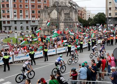 Los ciclistas pasan junto a manifestantes propalestina. 