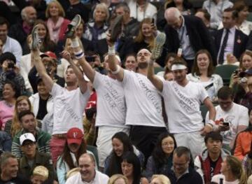 Los amigos de Marcus Willis sostienen sus zapatos en las gradas durante su partido contra el suizo Roger Federer