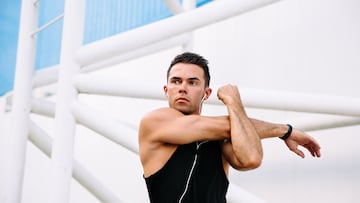 Hansome motivated sportsman listening to music in earphones while doing exercises for arms, wearing black t-shirt. Workout outdoors.