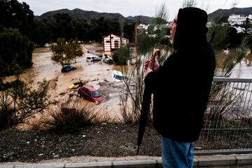 Un hombre observa cómo varios autos son arrastrados por el agua.