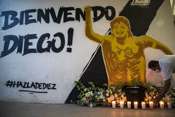 A man lights a candle below a mural of Diego Maradona as fans of the late Argentinian football legend gather outside Banorte Stadium in Culiacan, Sinaloa state, Mexico, on November 25, 2020. - Millions of fans paid tribute and Argentina was plunged into m