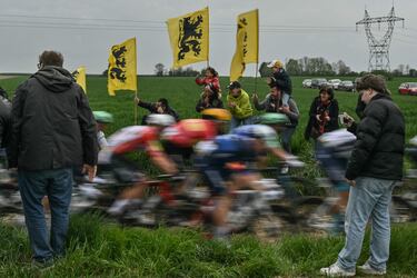 El grupo de ciclistas pasa junto a los espectadores que portan banderas del Movimiento Flamenco en una zona pavimentada durante la 122.ª edición de la clásica carrera ciclista de un día París-Roubaix, de 259,2 km entre Compiègne y Roubaix, en el norte de Francia.