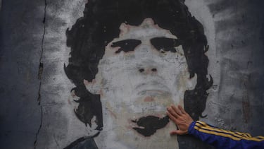 FILED - 25 November 2020, Argentina, Buenos Aires: A fan of the football club Boca Juniors puts his hand on a mural with the picture of the football star Diego Maradona on the day of his death. Argentina football great Diego Maradona has died at the age o