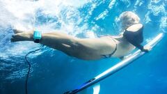 Una surfista realiza el pato abajo el agua con su tabla de surf y en bikini, con el gadget Goecho de detecci&oacute;n de tiburones enganchado a su tobillo. 