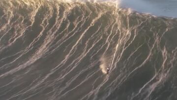 Un surfista vestido con una licra blanca surfea una ola gigante en Nazaré (Portugal) que marca las líneas blancas de la fuerza que tiene el mar. El labio, a punto de romper. Visto desde el aire. El 8 de enero del 2022.